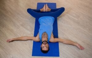 a man wearing blue doing reclined bound angle pose on a yoga mat