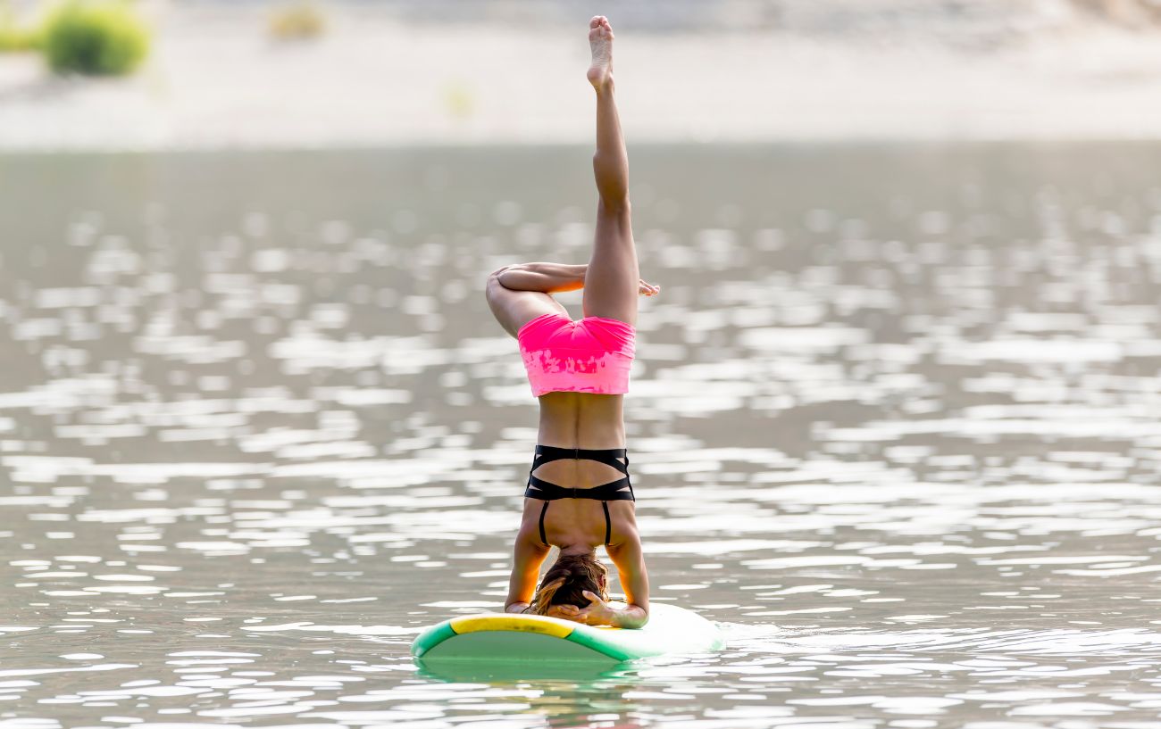 a woman doing a headstand on a paddle board 