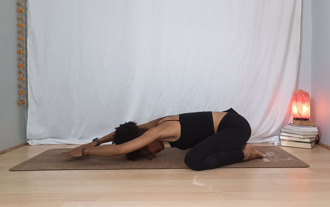 a woman doing wide legged child's pose variations with a salt lamp next to her