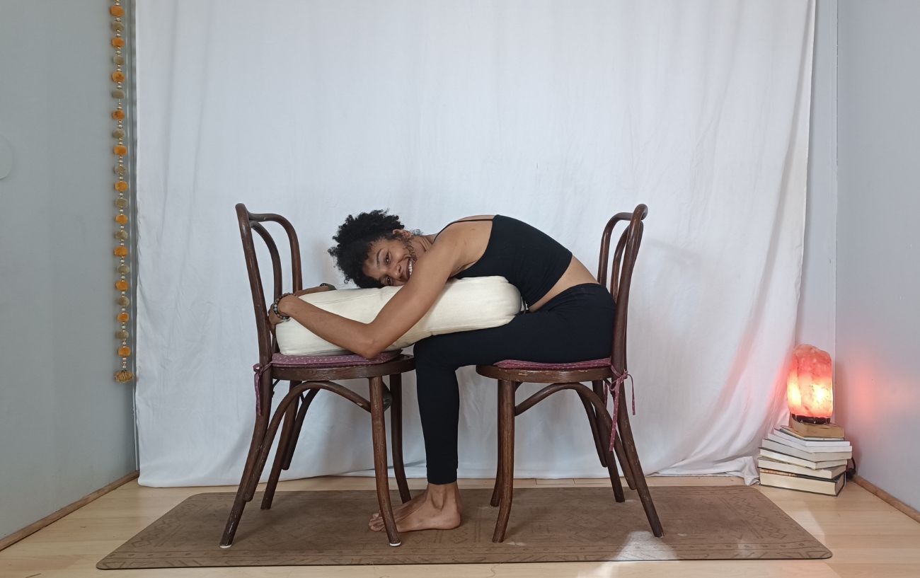 a woman doing child's pose on chairs with a bolster