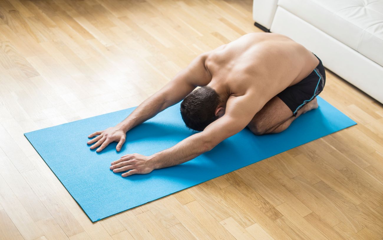 a man doing child's pose on a blue yoga mat