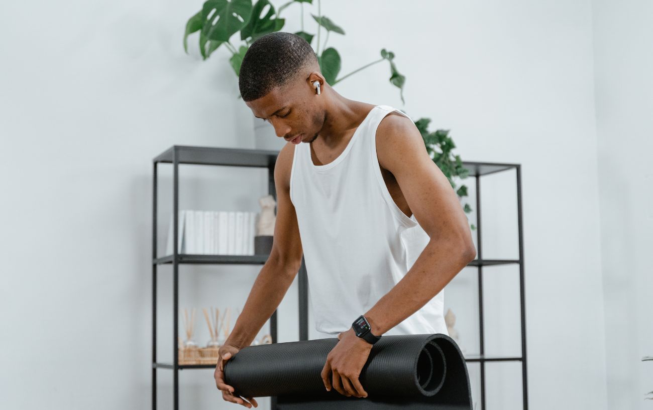 a man in a white tank unrolling a black yoga mat