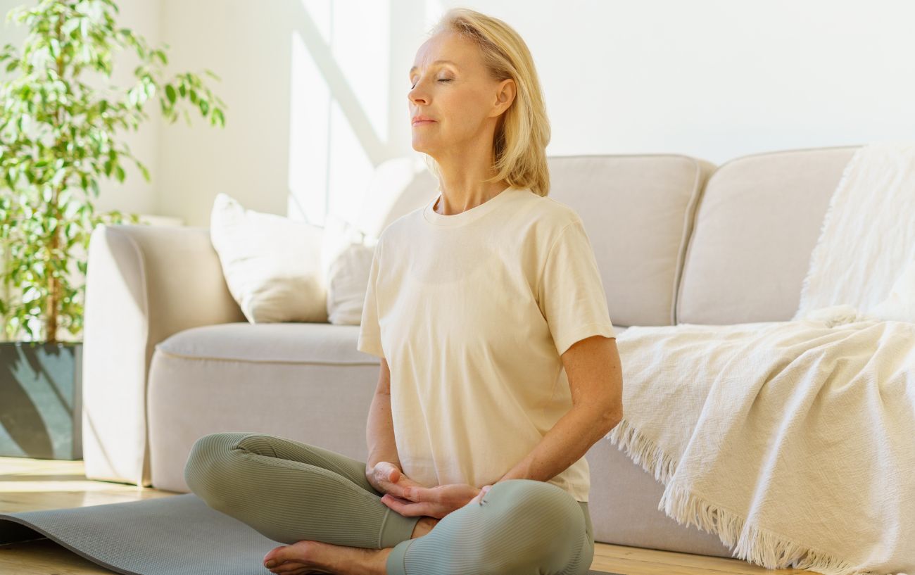 a woman doing breathwork sitting cross legged in front of a white sofa