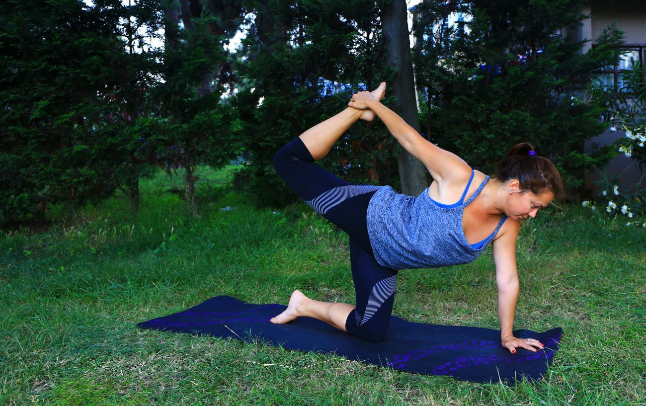 a woman doing tiger pose on a yoga mat in the park