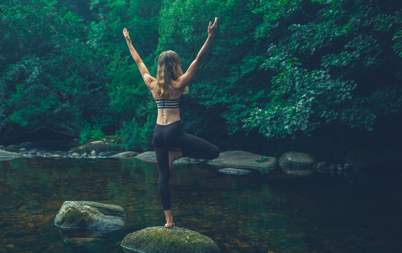 a woman in tree pose on a rock in a river