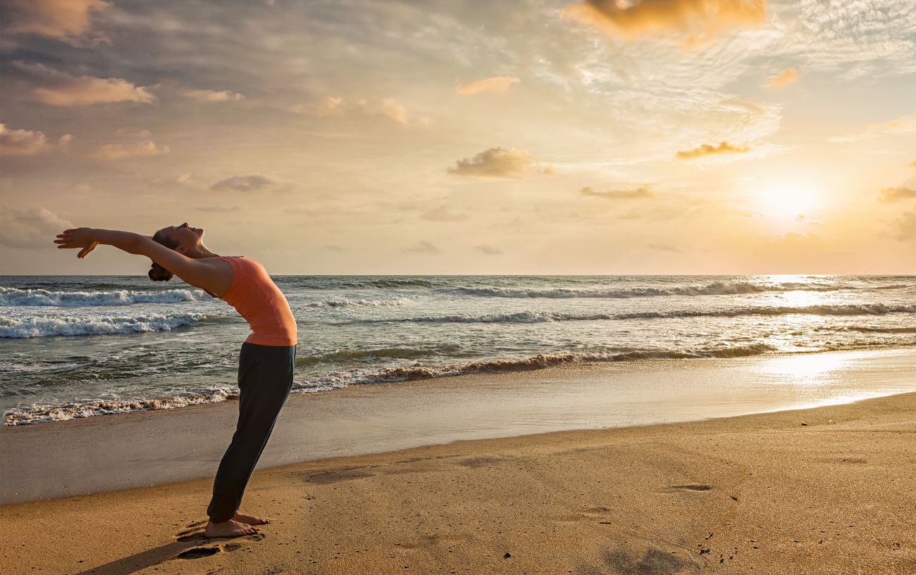 a woman doing sun salutations on a beach at sunset