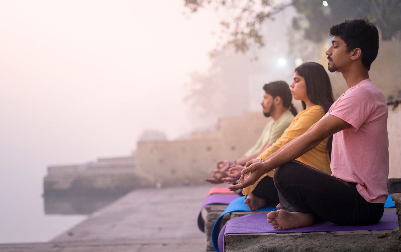 group of yogis sat meditating by a lake