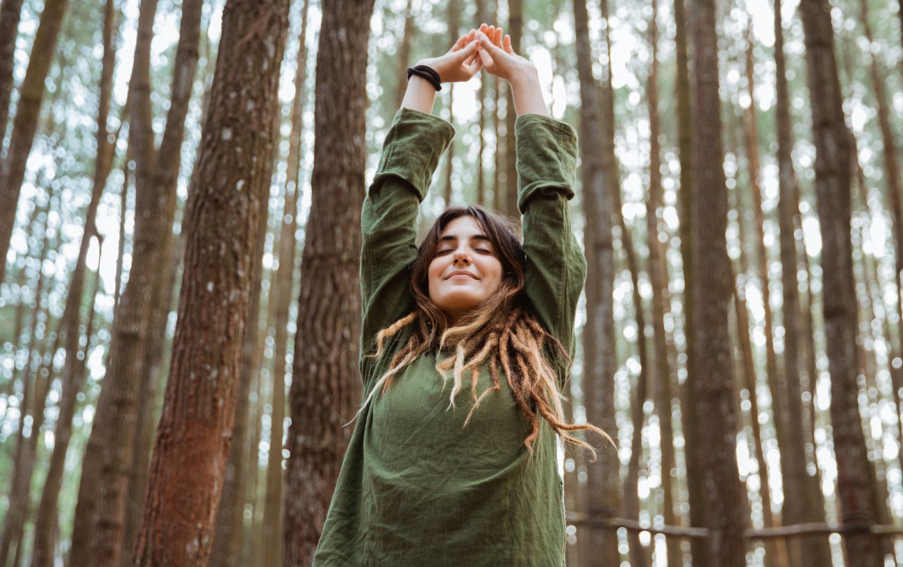 woman stretching her hands above her head in a forest