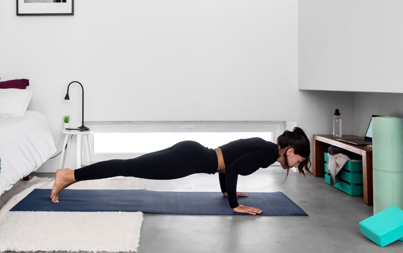 woman doing chaturanga dandasana/low plank in her bedroom on a mat