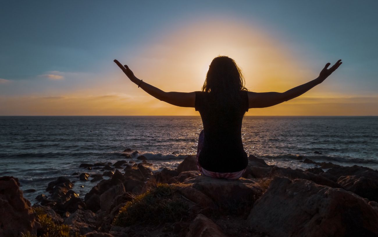 lady sat on the rocks by the sea opening her arms out wide