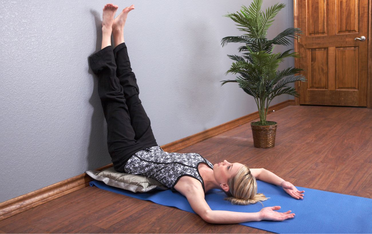 woman with her legs up the wall in her bedroom on a yoga mat