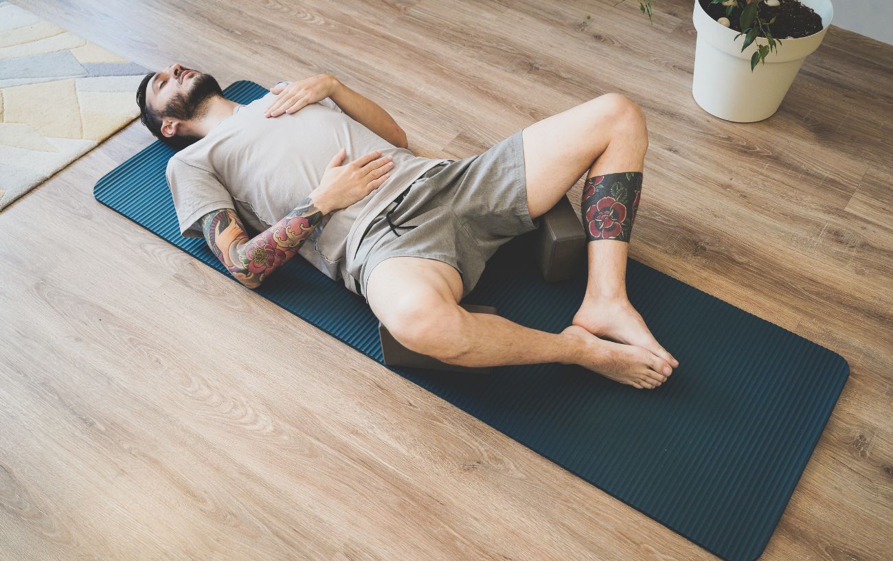 man practicing breathing exercises lying down on yoga mat 