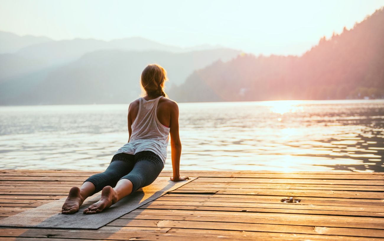 a woman doing upward facing dog yoga pose in front of a lake