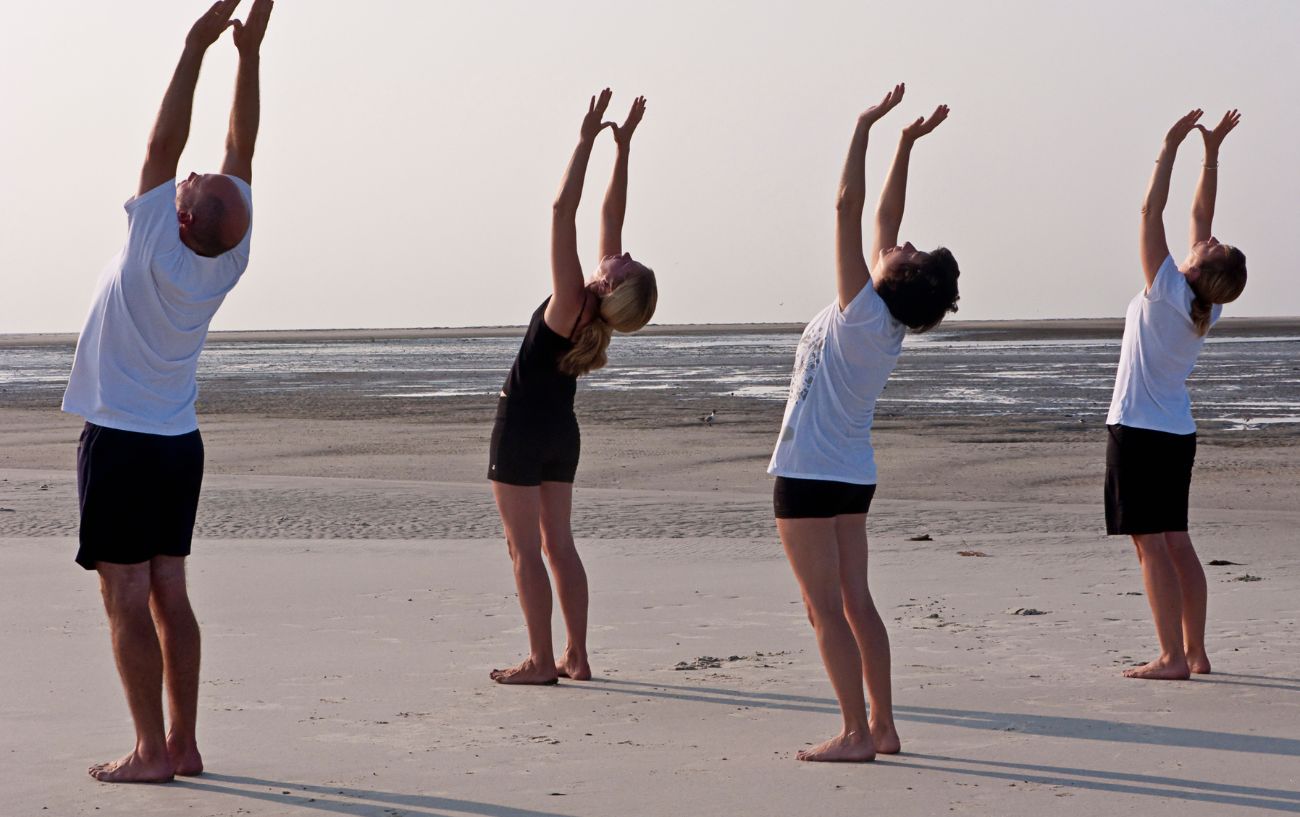 a group doing sun salutations on a beach