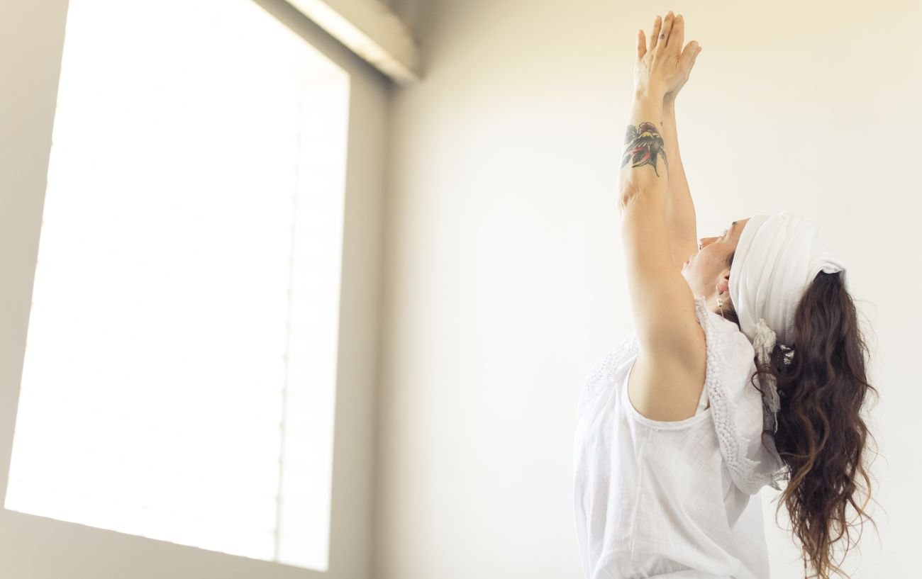 a woman wearing white doing yoga reaching up to the ceiling