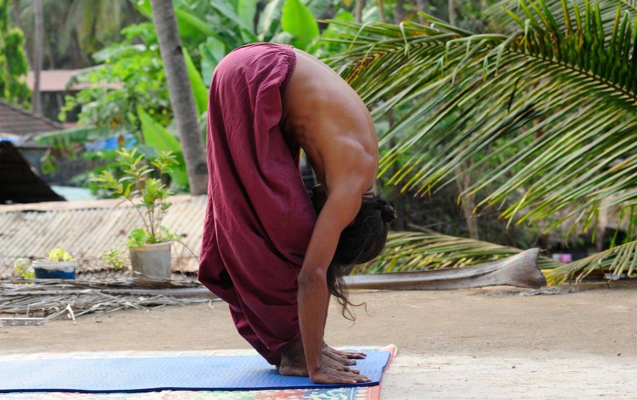 a man doing a forward fold on a yoga mat outside