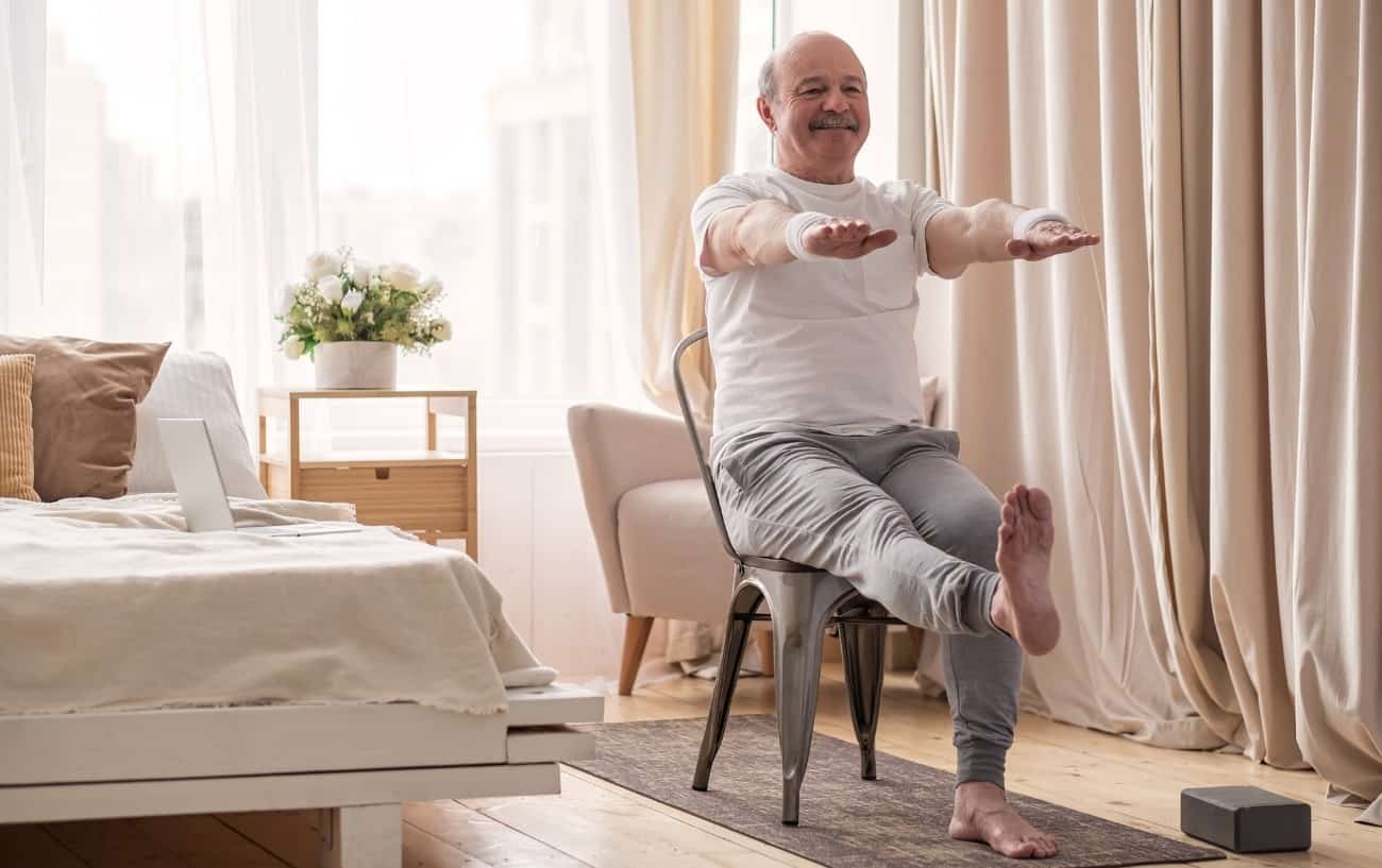 an older man practices a chair yoga routine in his bedroom