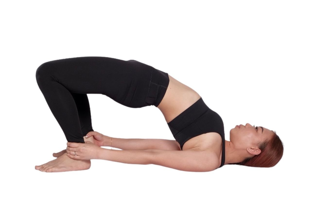 a woman wearing black yoga clothes in bridge pose holding her ankles