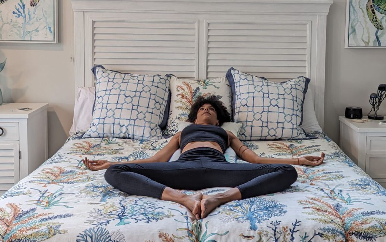 a woman doing reclining bound angle pose in black yoga clothes in bed