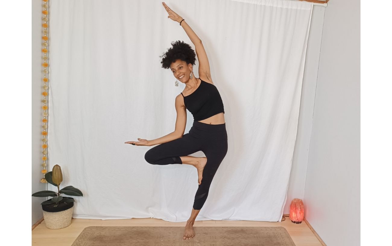 a woman doing a tree pose variation with a sideways lean against a white background