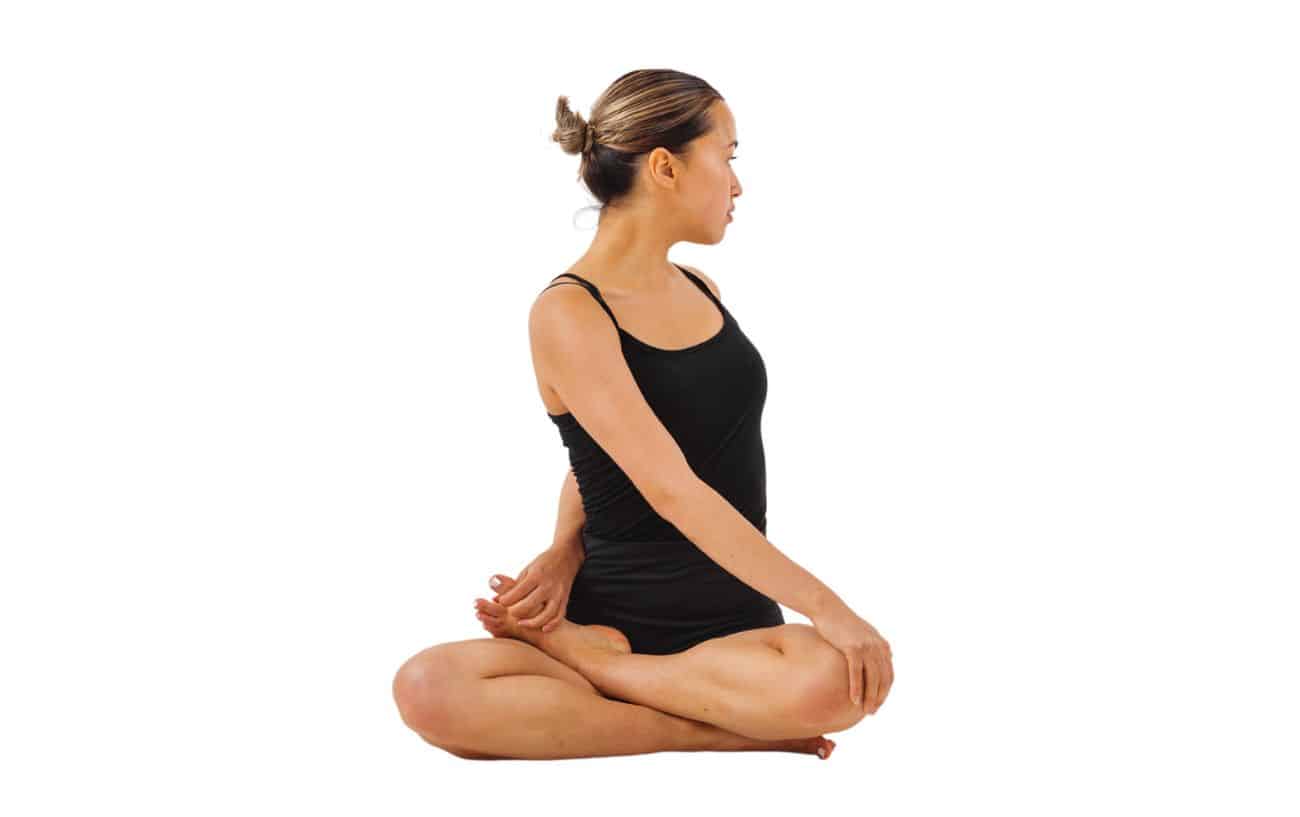 a woman wearing black yoga clothes does Bharadvaja’s Twist