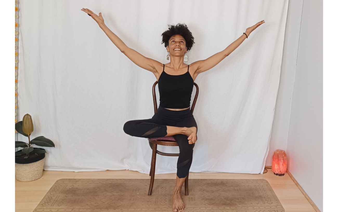 a woman doing a tree pose variation sitting on a chair against a white background