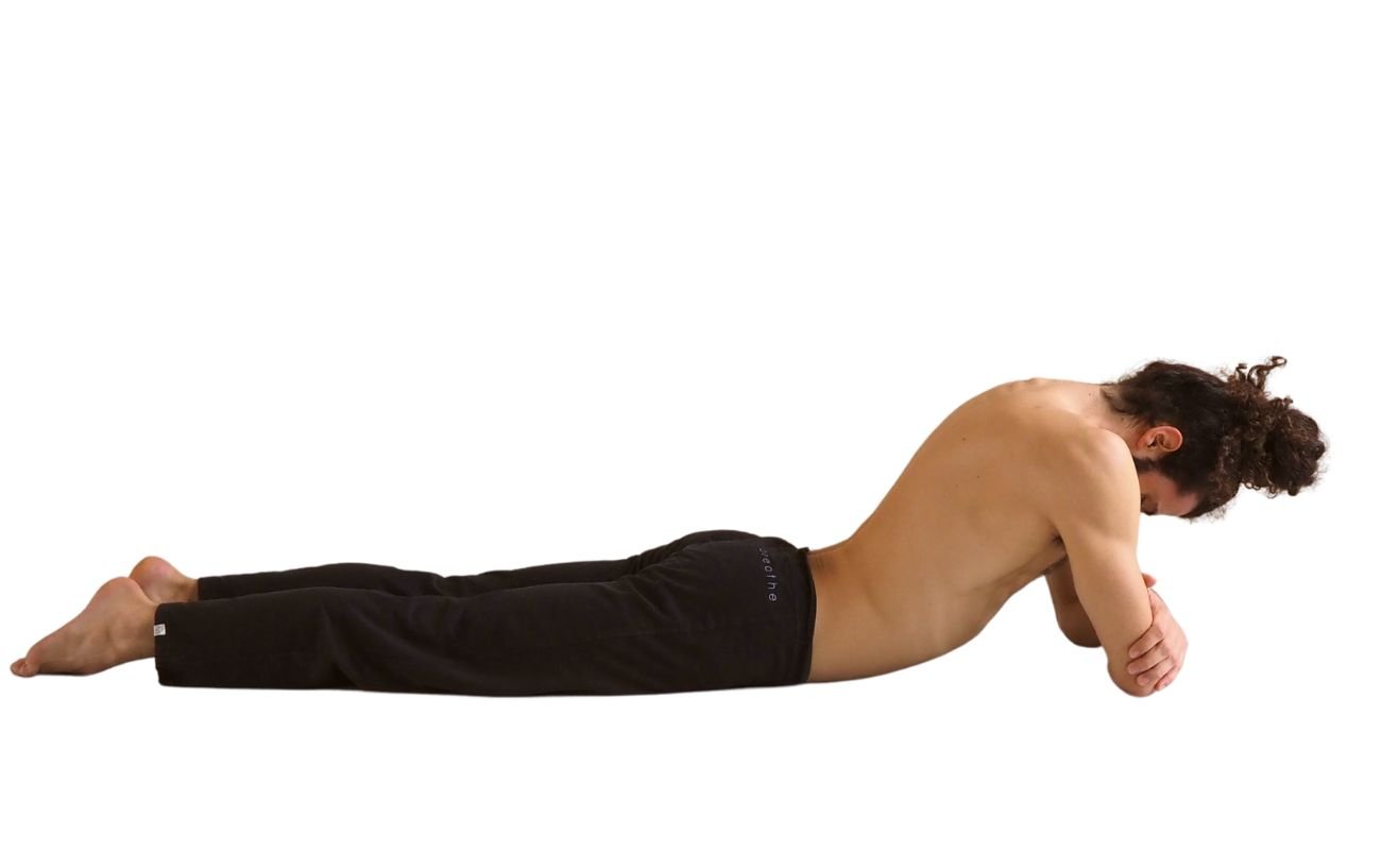 a man wearing black yoga trousers doing crocodile pose on his elbows