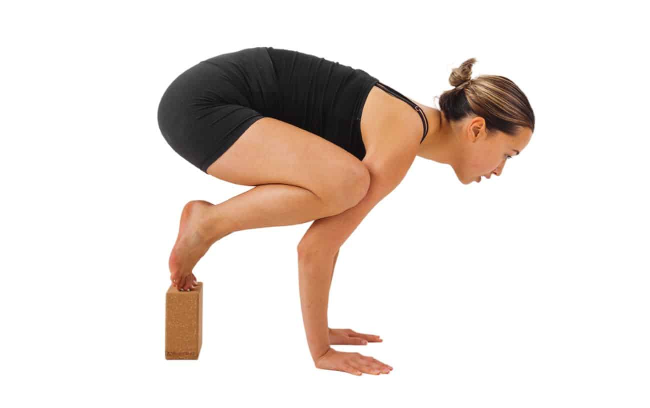 a woman wearing black yoga clothes doing crow pose with her feet on a block