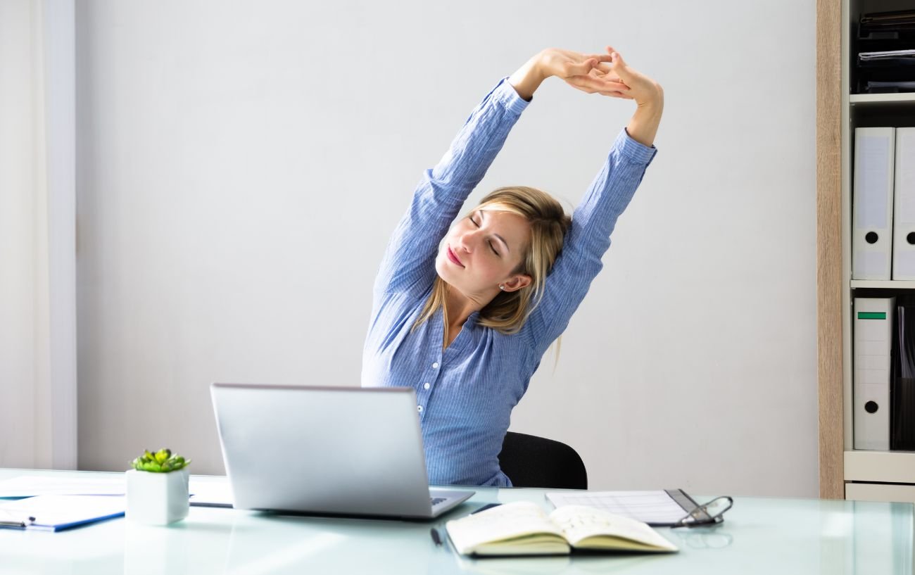 a woman doing desk yoga in a blue shirt