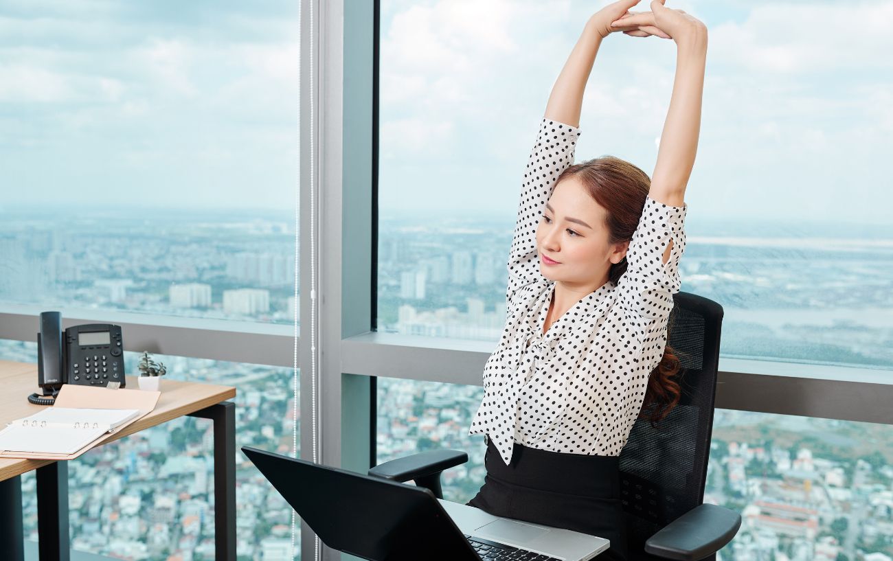 a woman stretching at her desk overlooking a city