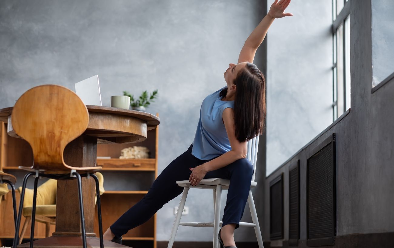 a woman in a blue top doing chair yoga in an office