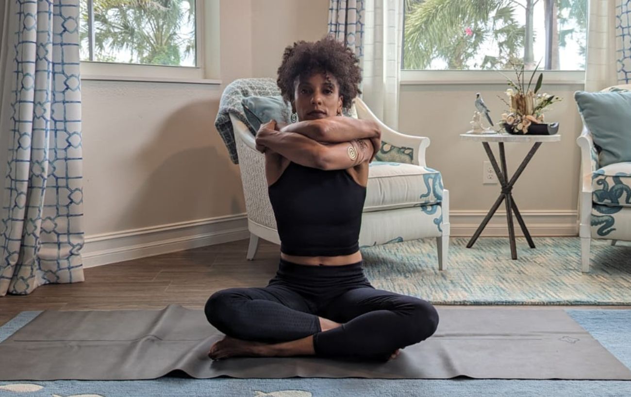 a woman wearing black yoga clothes doing yoga neck stretches cross legged in her living room