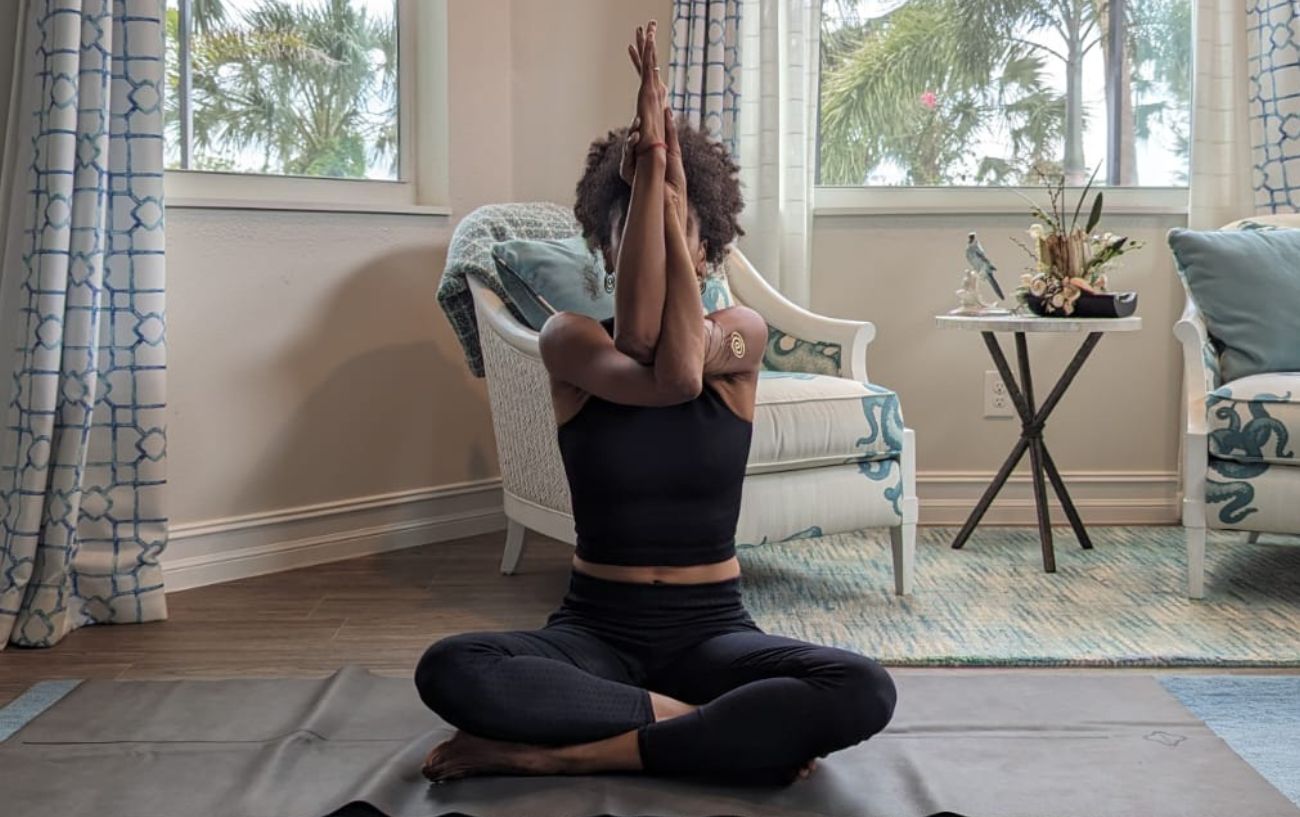 a woman wearing black yoga clothes doing yoga neck stretches cross legged in her living room