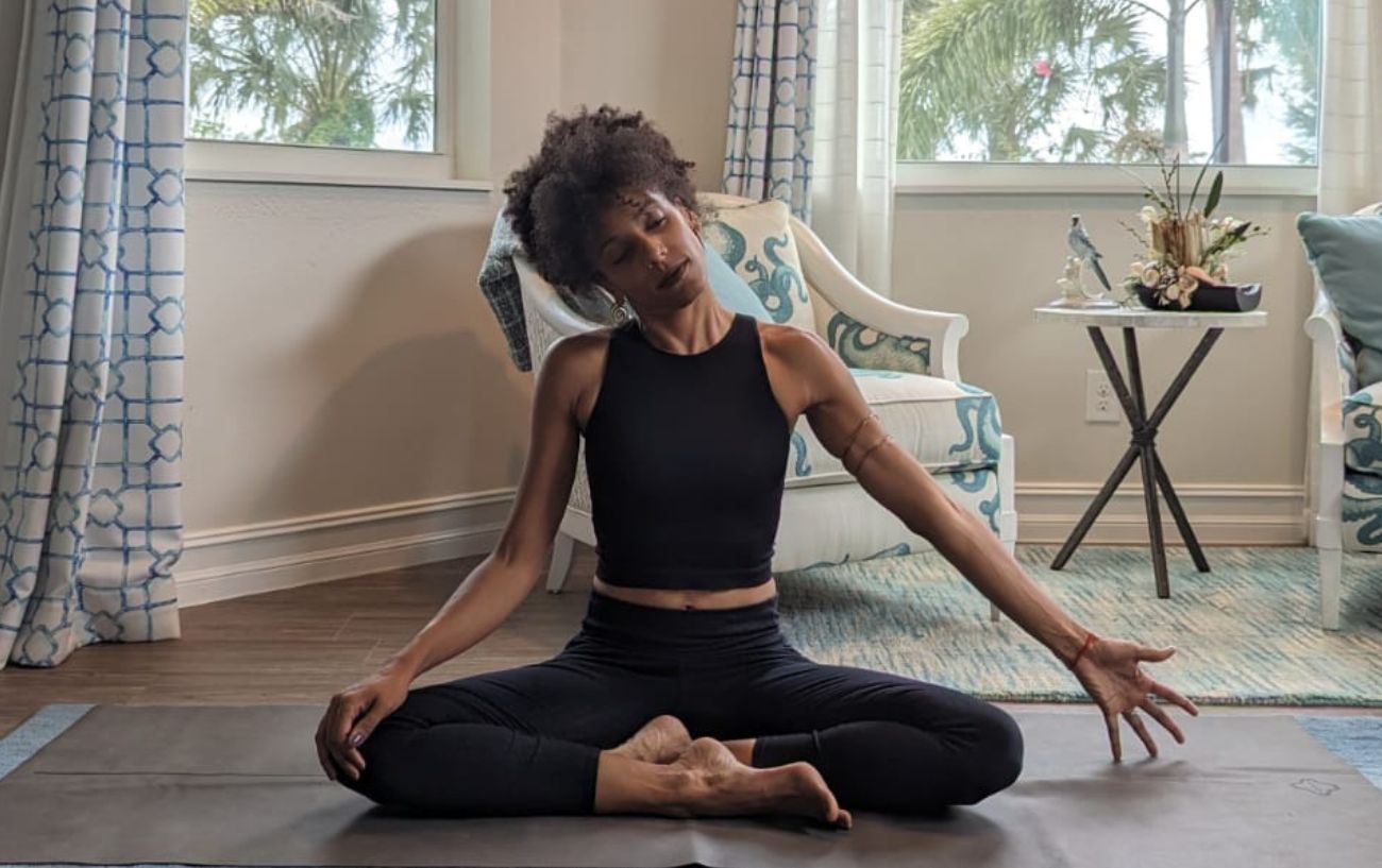 a woman wearing black yoga clothes doing yoga neck stretches cross legged in her living room