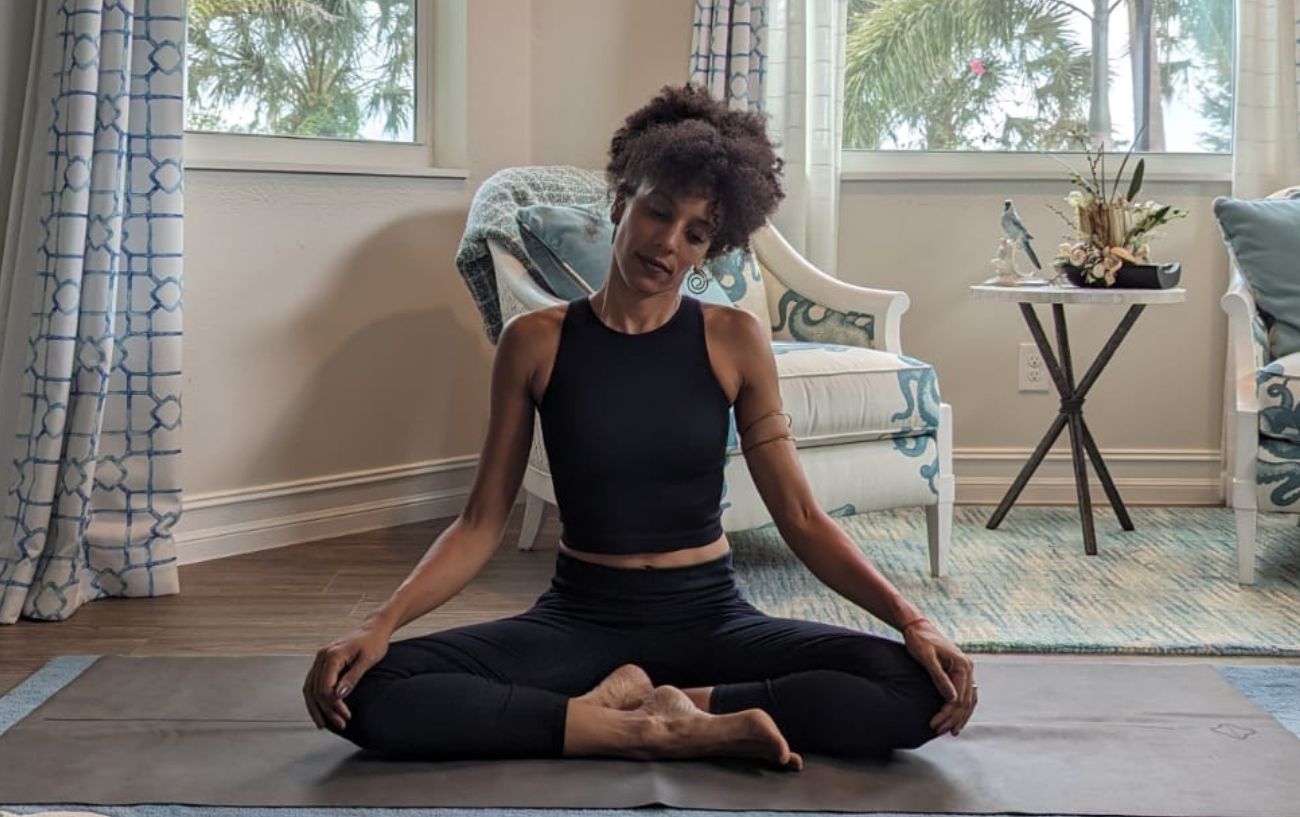 a woman wearing black yoga clothes doing yoga neck stretches cross legged in her living room