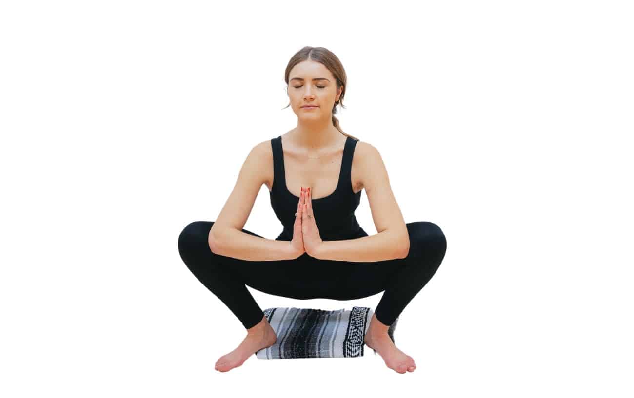 a woman does garland pose malasana with a blanket under her heels