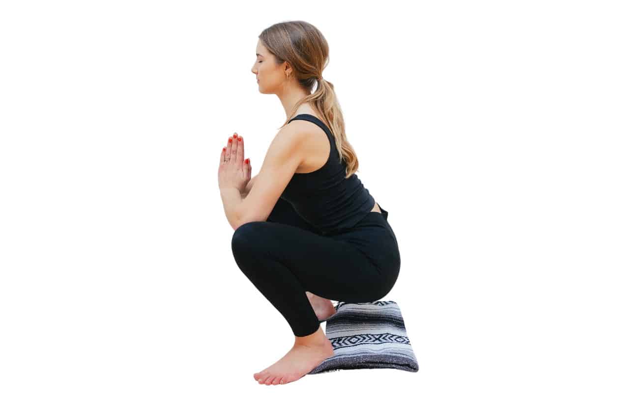 a woman does garland pose malasana with her ankles on a blanket