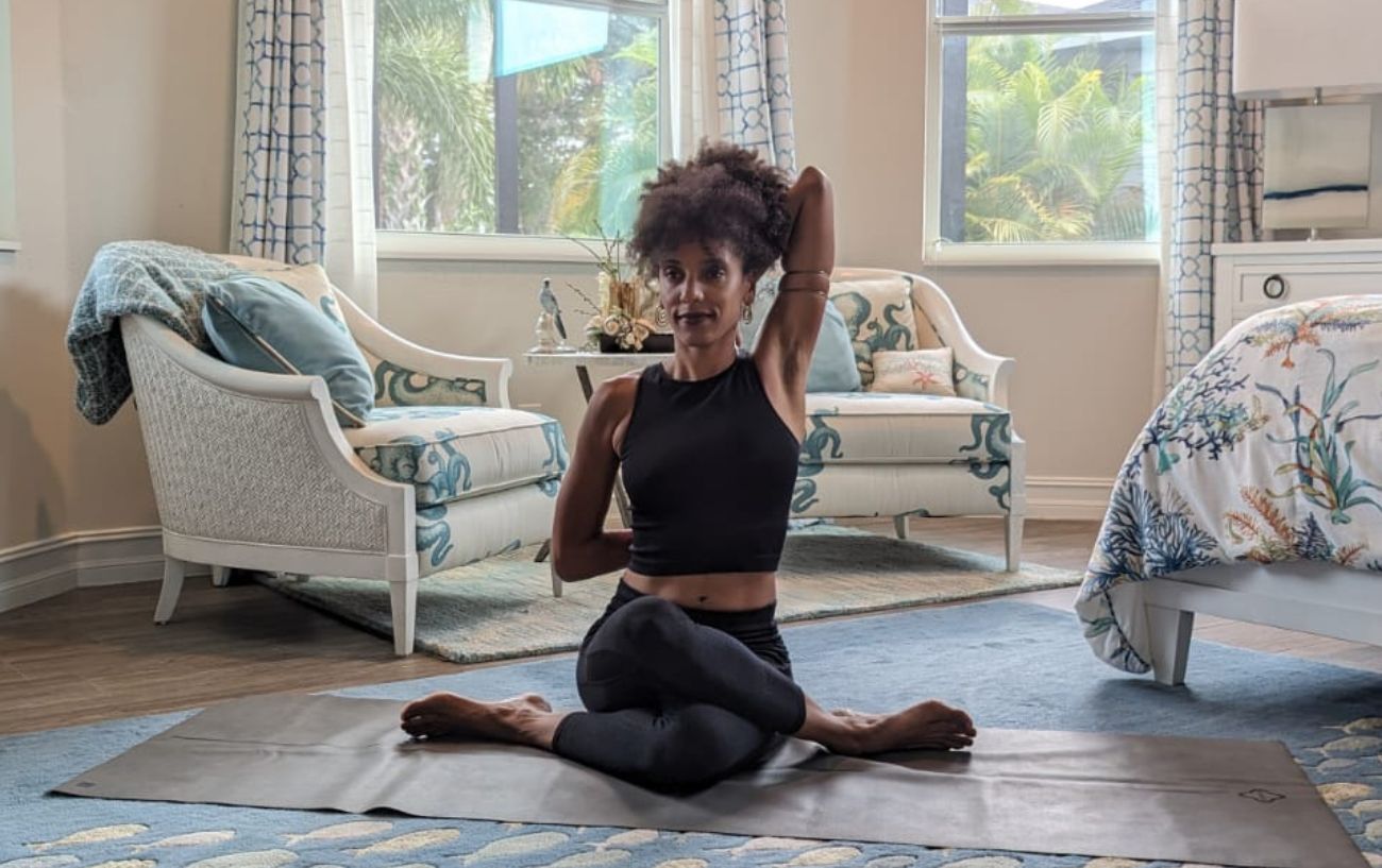 a woman doing cow face pose in black yoga clothes in a living room