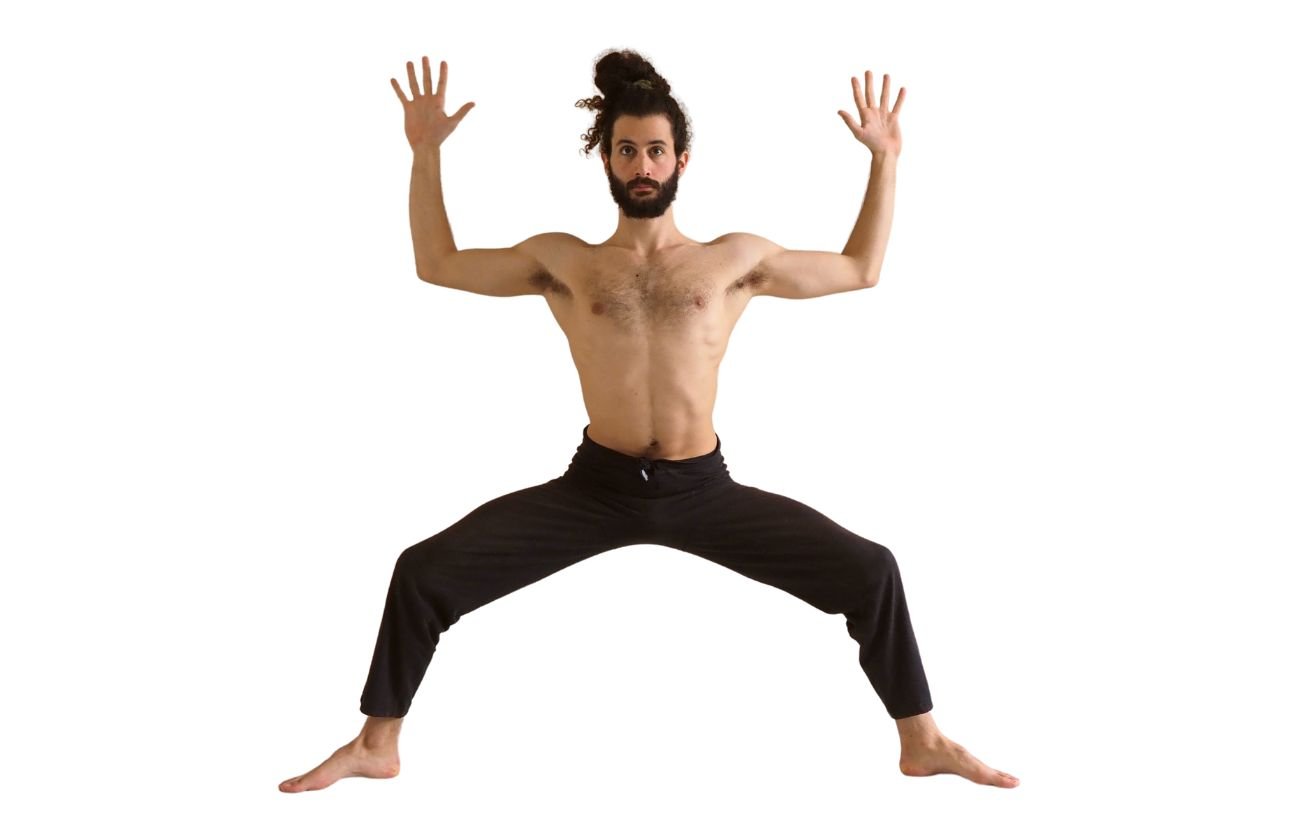 a man wearing black yoga trousers doing goddess pose