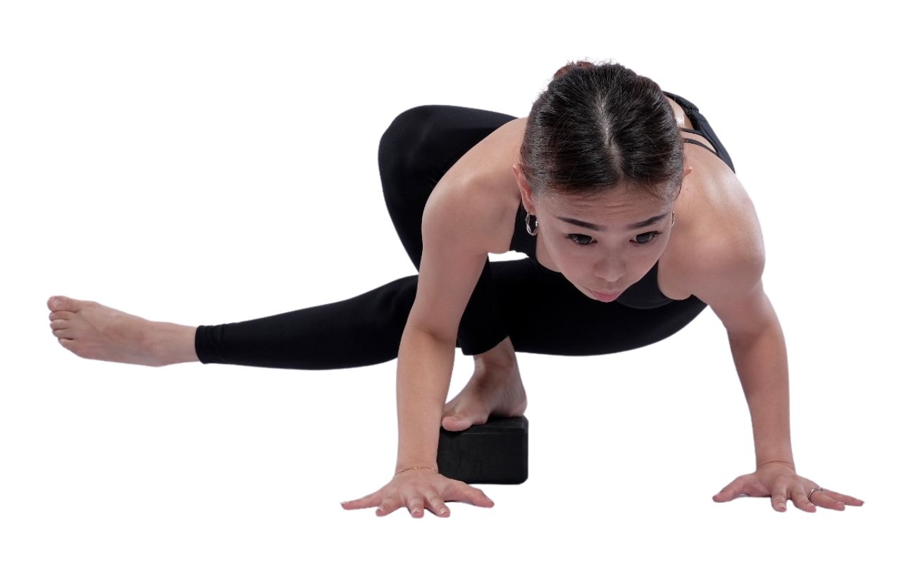 a woman wearing black yoga clothes doing grasshopper pose with a foot on a block