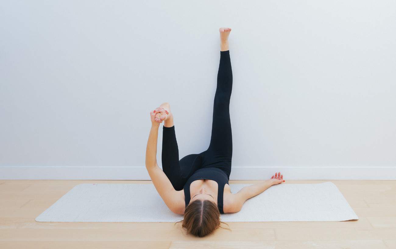 woman doing a half happy baby pose with a leg up the wall