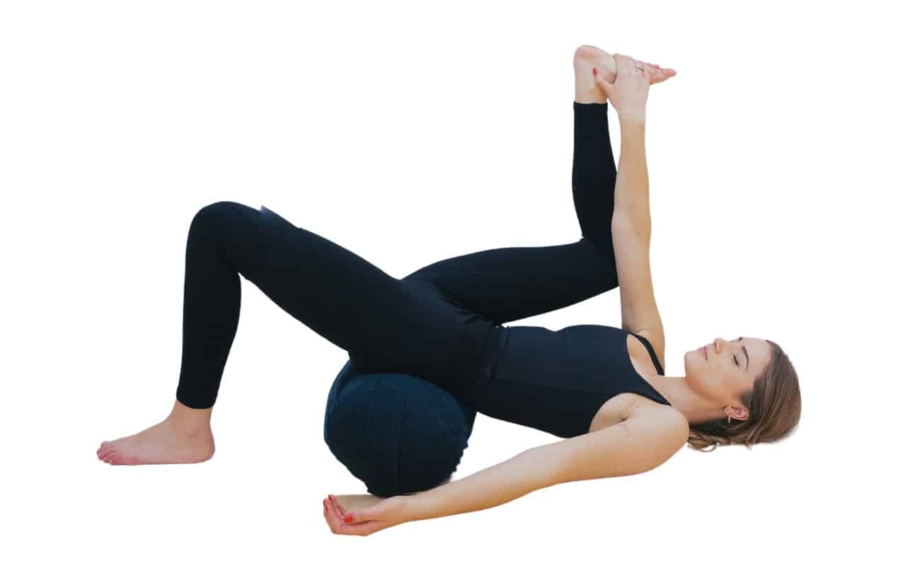 woman doing a half happy baby pose with a bolster