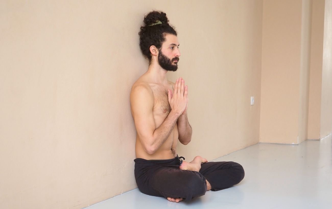 a man wearing black yoga trousers doing half lotus pose against a wall