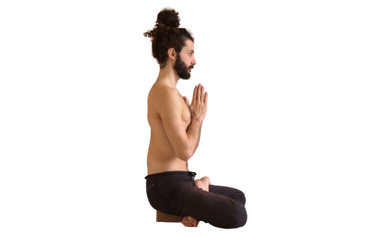 a man wearing black yoga trousers doing half lotus pose on a block