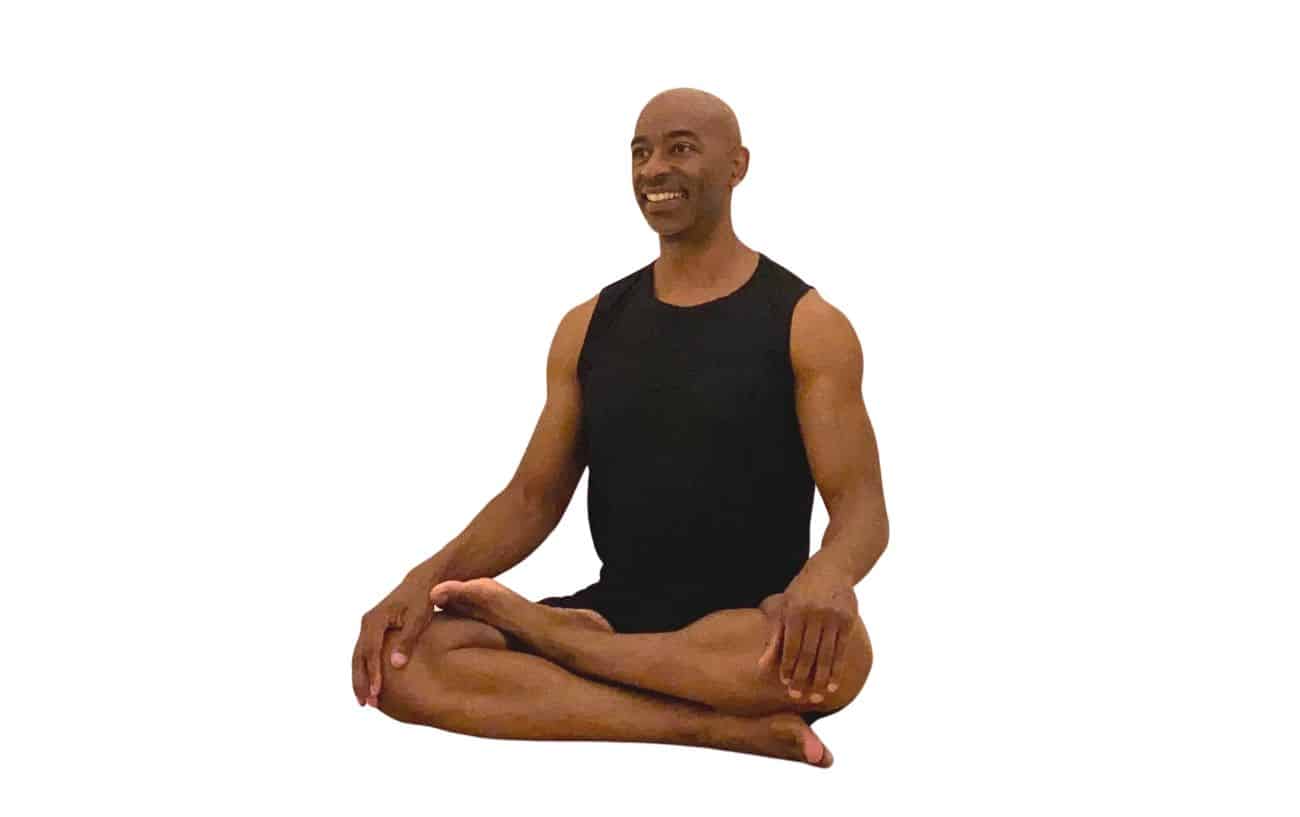 a man wearing black yoga clothes sitting in half lotus pose