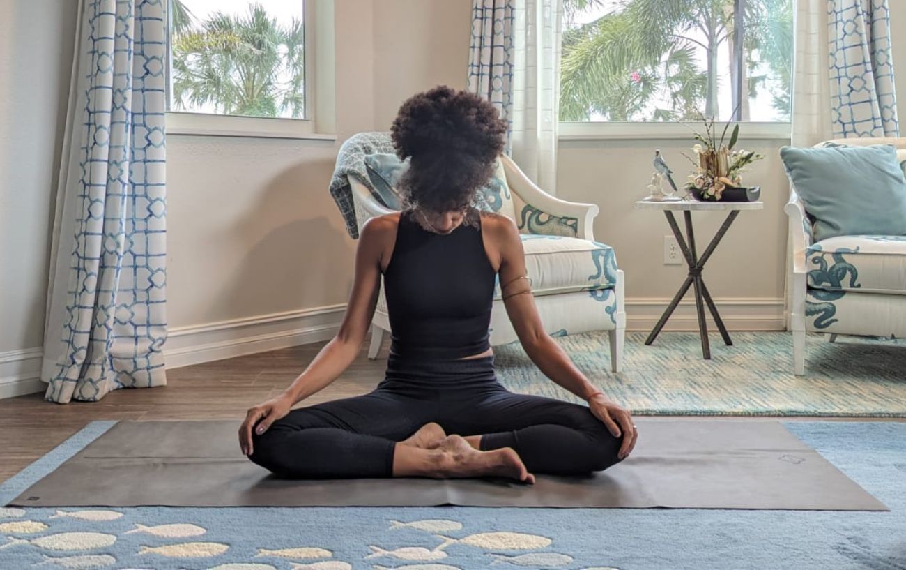 a woman wearing black yoga clothes doing neck stretches cross legged in her living room