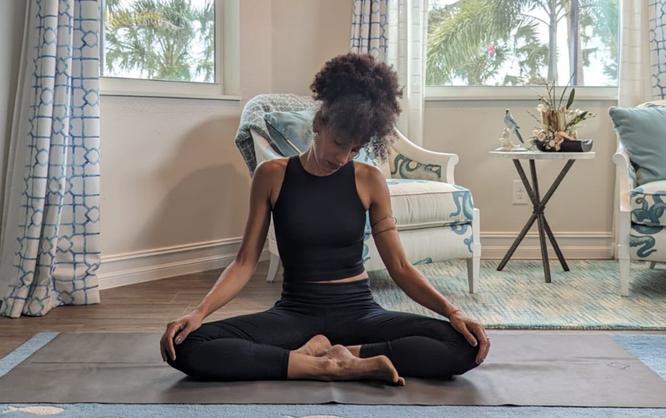 a woman wearing black yoga clothes doing neck stretches cross legged in her living room