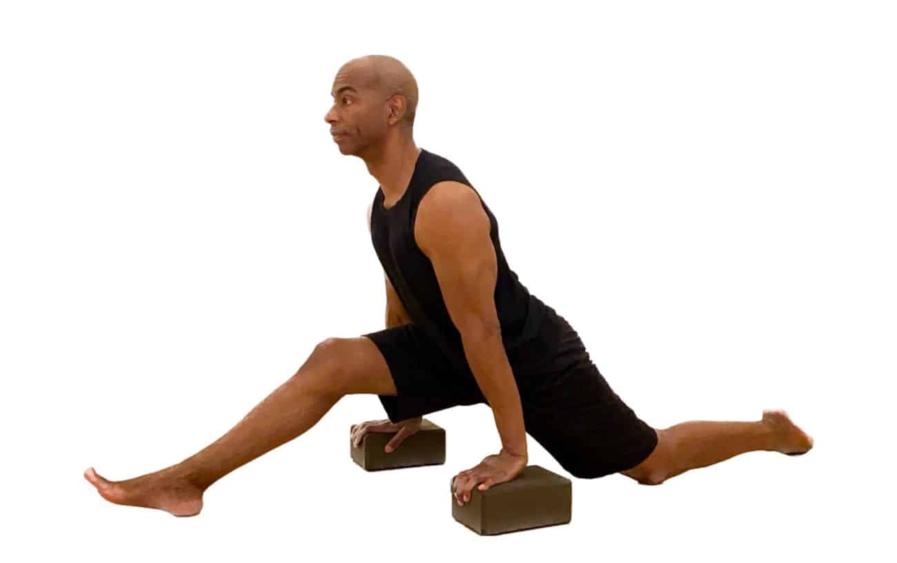 a man wearing all black yoga clothes does hald splits pose with blocks