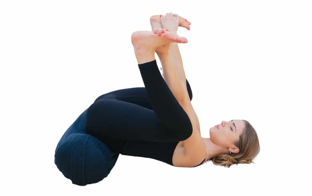 woman doing a happy baby pose with bolster under her hips