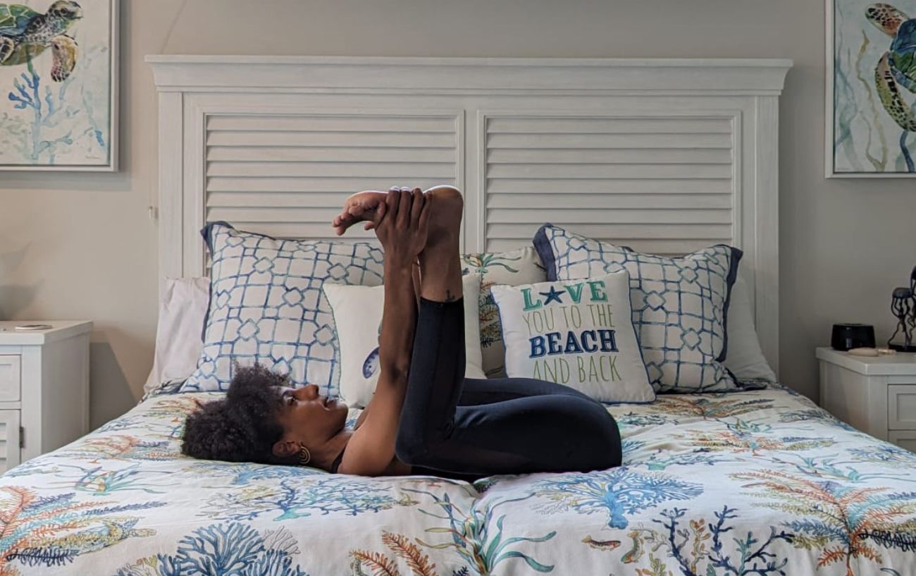 a woman doing happy baby pose in black yoga clothes in bed